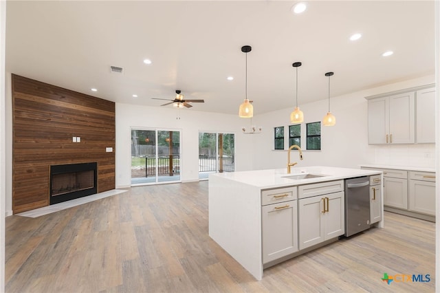 kitchen featuring light hardwood / wood-style flooring, sink, a kitchen island with sink, pendant lighting, and a large fireplace