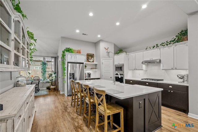 kitchen featuring a kitchen island with sink, under cabinet range hood, stainless steel appliances, white cabinetry, and a kitchen breakfast bar