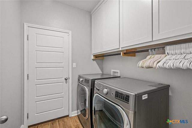 clothes washing area featuring light wood finished floors, separate washer and dryer, cabinet space, and baseboards