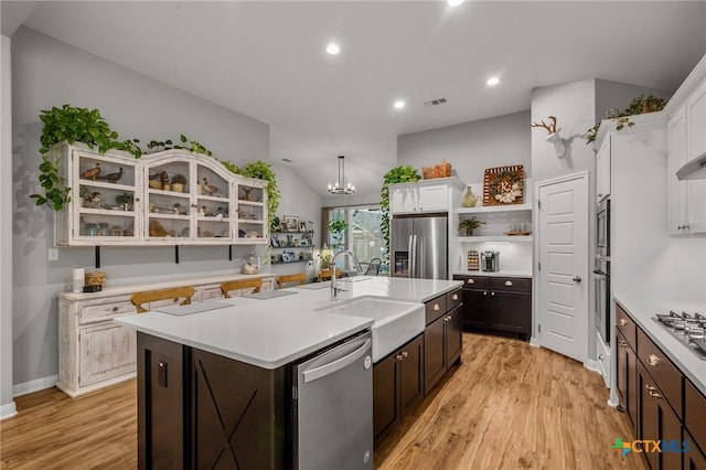 kitchen featuring light countertops, hanging light fixtures, appliances with stainless steel finishes, a kitchen island with sink, and dark brown cabinets