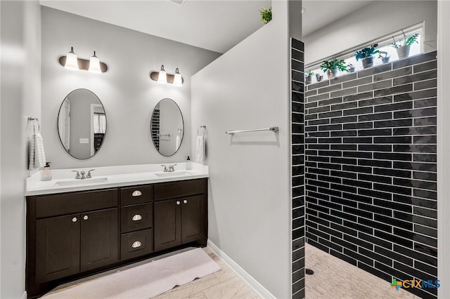 full bathroom with a walk in shower, double vanity, a sink, and baseboards