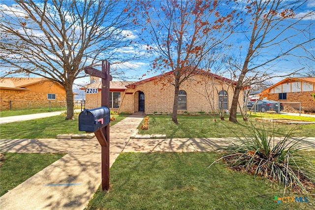 view of front of property with brick siding, a front lawn, and fence