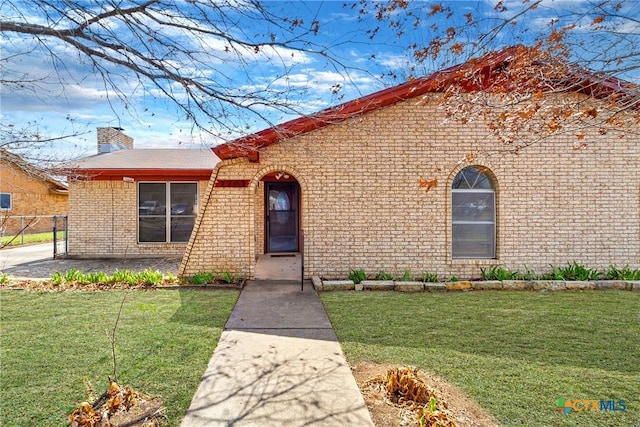 view of front facade with brick siding, a chimney, a front yard, and fence