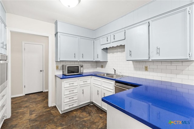 kitchen with a sink, tasteful backsplash, dark countertops, appliances with stainless steel finishes, and white cabinets