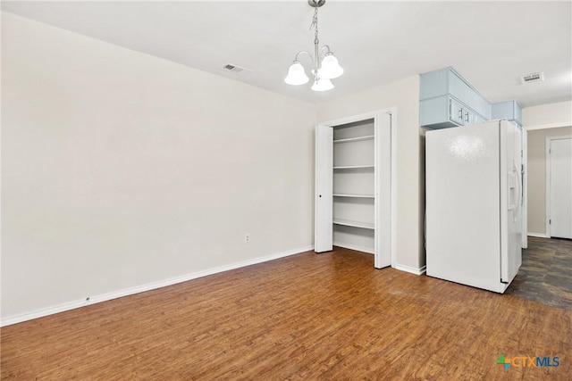 unfurnished bedroom featuring dark wood finished floors, visible vents, white refrigerator with ice dispenser, and a chandelier