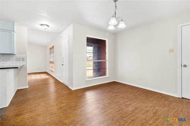 unfurnished dining area with an inviting chandelier, dark wood-type flooring, and baseboards