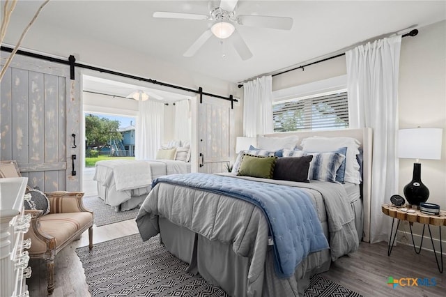 bedroom featuring a barn door, wood finished floors, a ceiling fan, and multiple windows