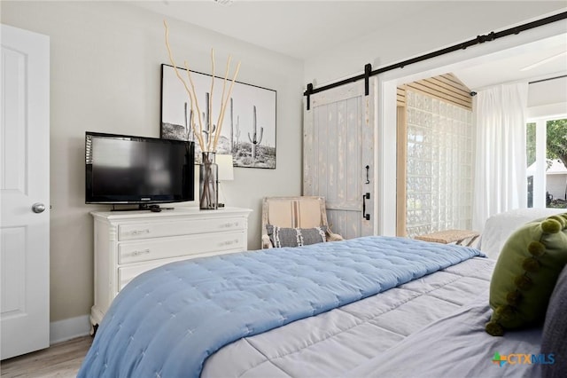 bedroom with baseboards, wood finished floors, a barn door, and access to exterior
