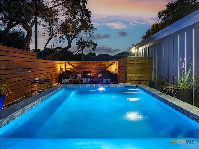 pool at dusk with a fenced backyard and a fenced in pool
