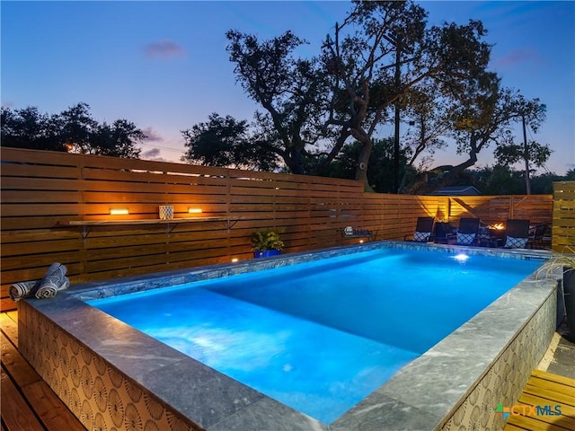 pool at dusk with a fenced backyard and a fenced in pool
