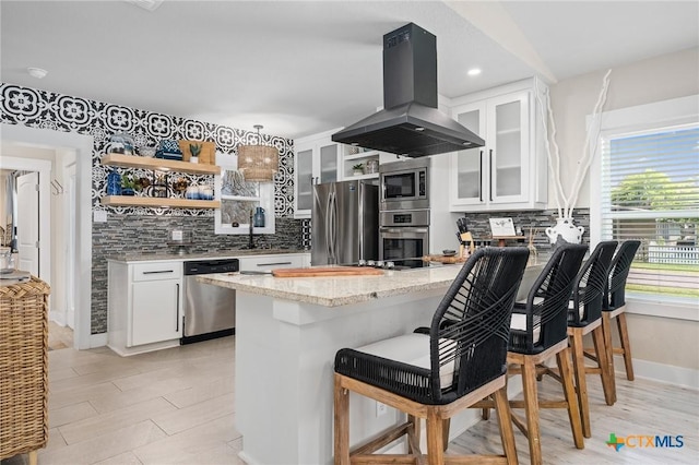 kitchen featuring stainless steel appliances, a peninsula, tasteful backsplash, island range hood, and open shelves
