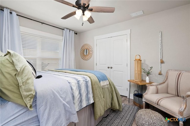 bedroom with a ceiling fan, wood finished floors, visible vents, and a closet