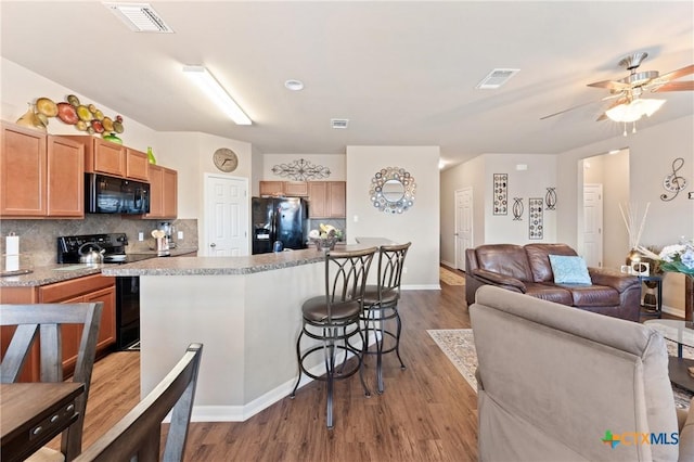 kitchen featuring wood finished floors, a kitchen breakfast bar, visible vents, and black appliances