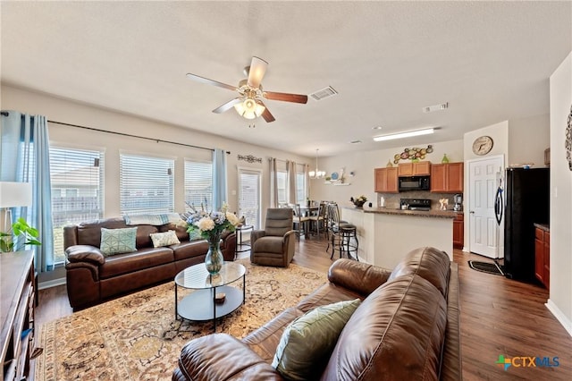 living room with dark wood-style flooring, visible vents, and ceiling fan with notable chandelier