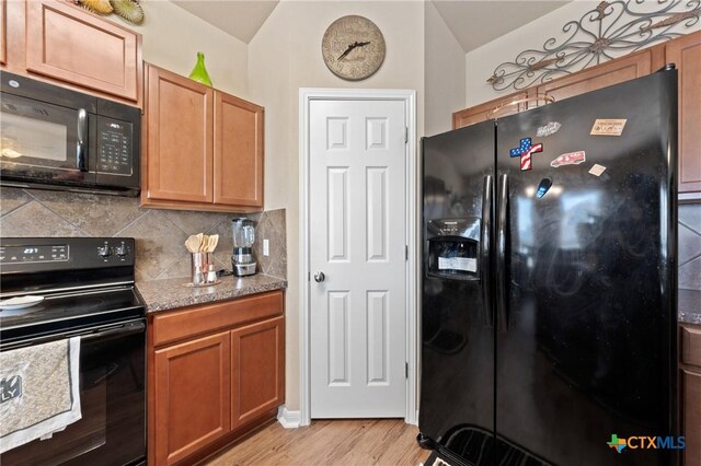 kitchen featuring tasteful backsplash, light wood-type flooring, vaulted ceiling, and black appliances