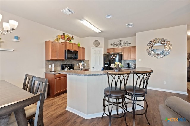 kitchen featuring backsplash, wood finished floors, visible vents, black appliances, and a kitchen bar