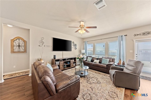living area with baseboards, wood finished floors, visible vents, and ceiling fan