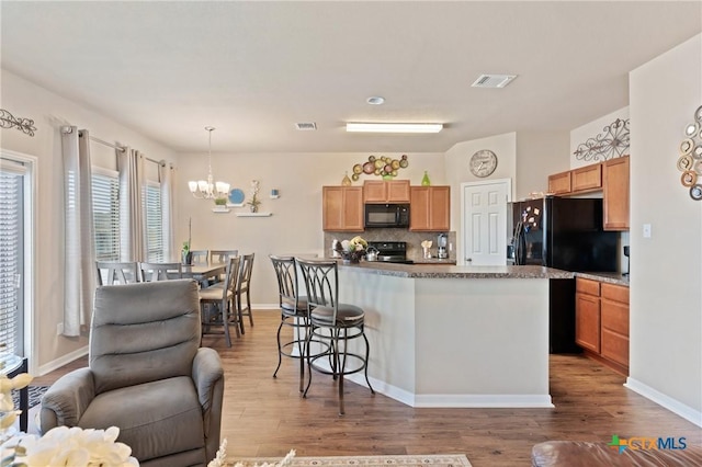 kitchen featuring an inviting chandelier, visible vents, a kitchen breakfast bar, and black appliances