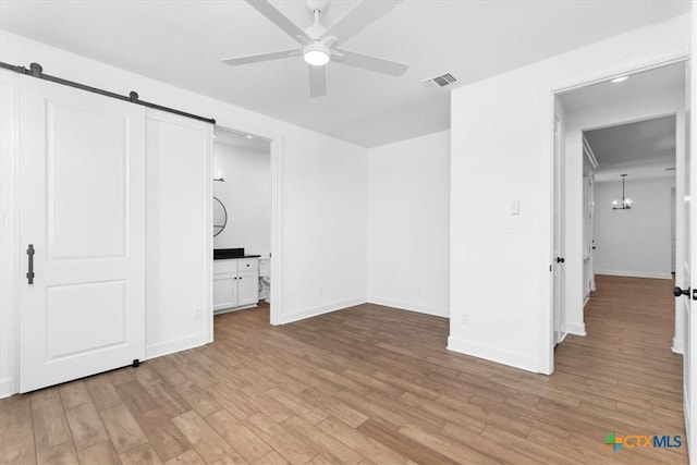 unfurnished bedroom featuring a barn door, an inviting chandelier, and light hardwood / wood-style flooring