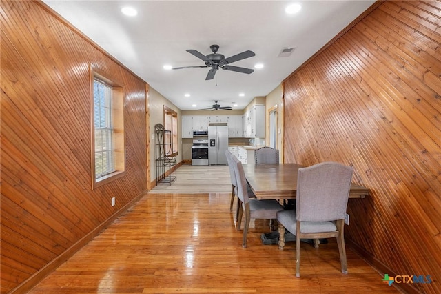 dining space with light hardwood / wood-style flooring, ceiling fan, and wooden walls