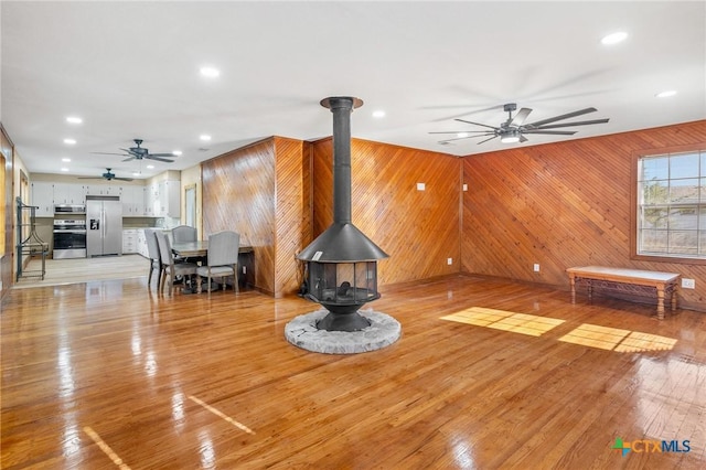 living room with a wood stove, ceiling fan, and light hardwood / wood-style floors