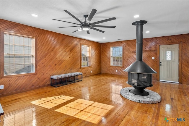 unfurnished living room with a wood stove, ceiling fan, wood walls, and hardwood / wood-style flooring