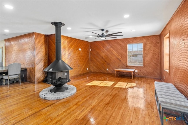 living room with a wood stove, ceiling fan, and wooden walls