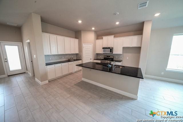 kitchen with backsplash, stainless steel appliances, a kitchen island with sink, and white cabinets