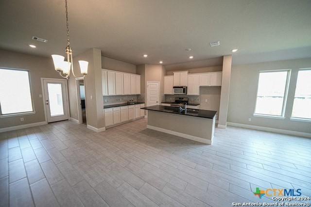 kitchen with appliances with stainless steel finishes, decorative light fixtures, white cabinetry, a chandelier, and a center island with sink