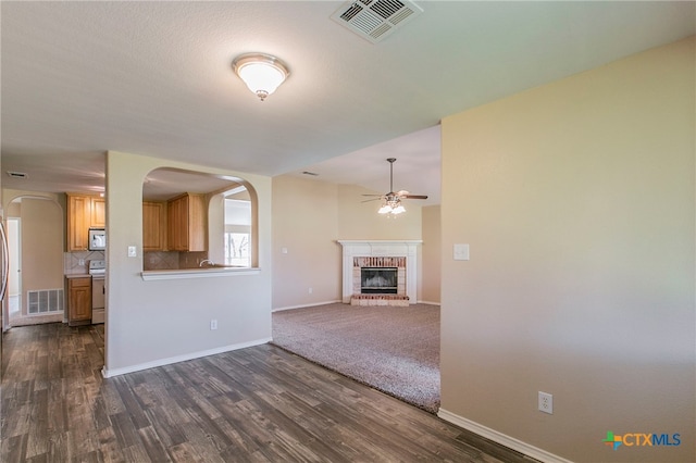 unfurnished living room with a fireplace, ceiling fan, and dark hardwood / wood-style flooring