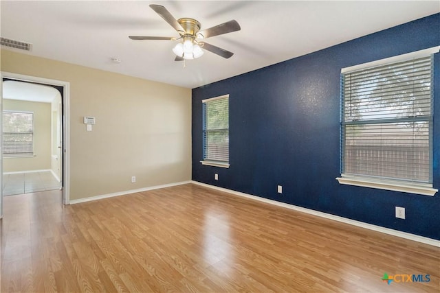 empty room with a wealth of natural light, visible vents, wood finished floors, and a ceiling fan
