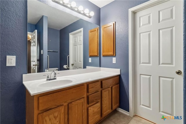 bathroom with tile patterned floors, toilet, a textured wall, and vanity