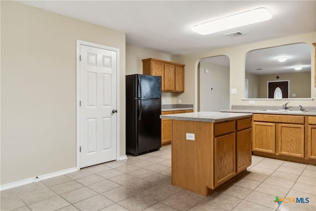 kitchen with arched walkways, freestanding refrigerator, light countertops, a sink, and visible vents