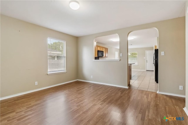 empty room with baseboards, arched walkways, and light wood finished floors