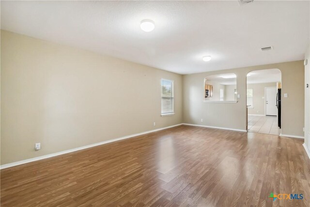 unfurnished room featuring baseboards, arched walkways, and light wood-style floors