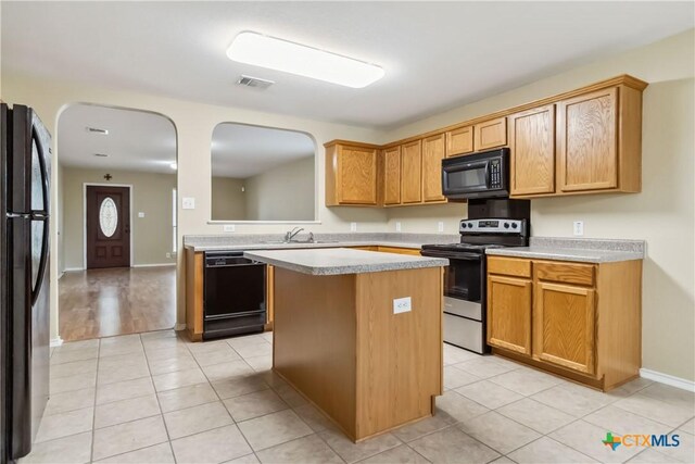 kitchen with black appliances, light tile patterned floors, light countertops, and a center island