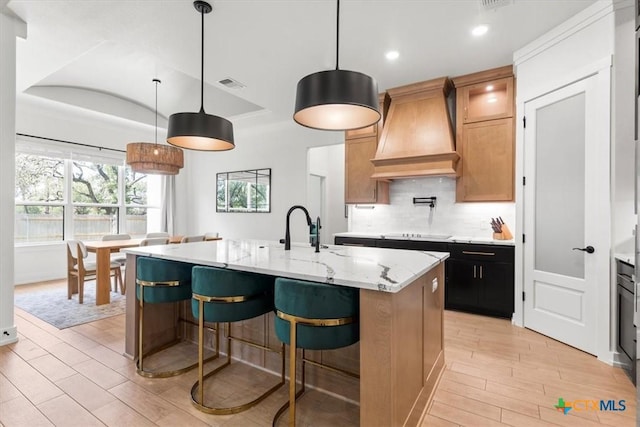 813 Eagle Heights Dr, Salado, TX 76571 - kitchen with custom range hood, light wood-type flooring, black electric stovetop, an island with sink, and light stone counters