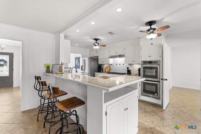 kitchen with visible vents, a breakfast bar, a ceiling fan, backsplash, and stainless steel appliances