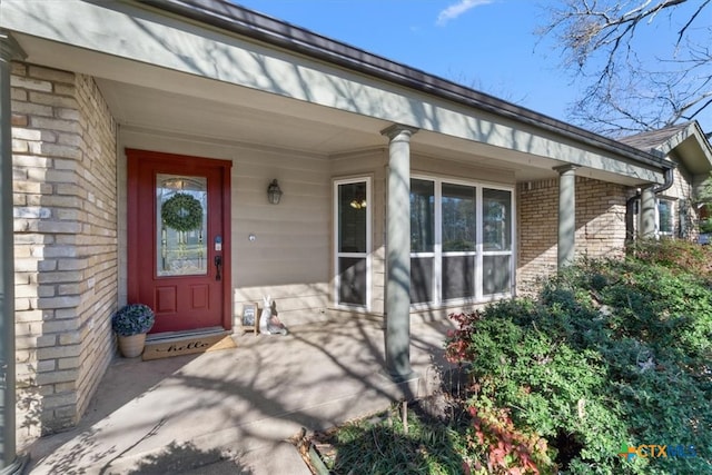 entrance to property featuring a porch and brick siding