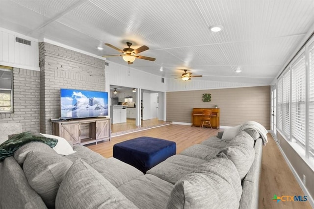 living room featuring visible vents, brick wall, baseboards, light wood-style floors, and a ceiling fan