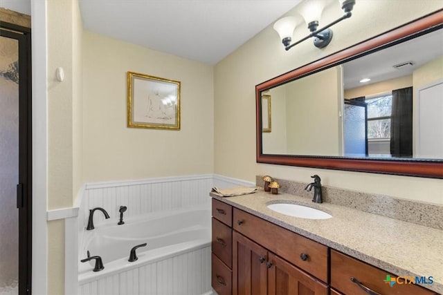 bathroom with a wainscoted wall, visible vents, vanity, and a garden tub