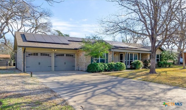 ranch-style home featuring brick siding, a front lawn, concrete driveway, roof mounted solar panels, and a garage