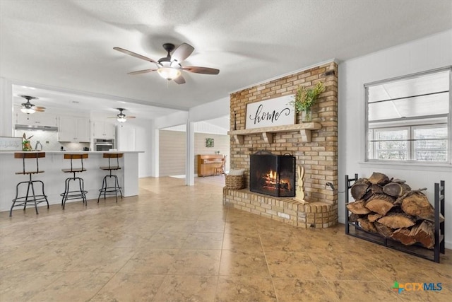 living room with a fireplace, a textured ceiling, and a ceiling fan