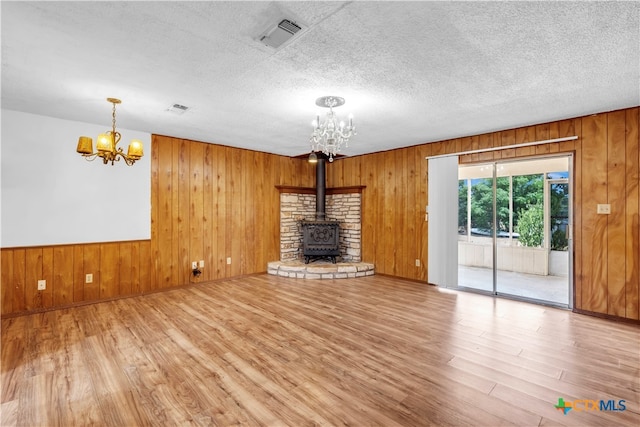 unfurnished living room with a wood stove, wood-type flooring, a textured ceiling, and wood walls