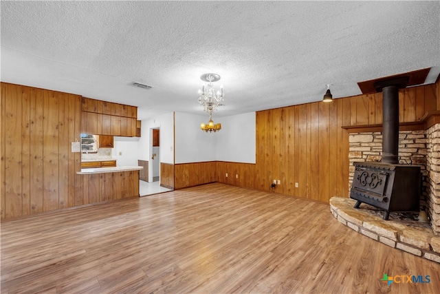 unfurnished living room featuring a textured ceiling, wooden walls, a wood stove, and light hardwood / wood-style flooring