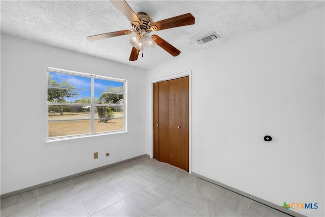 unfurnished bedroom featuring ceiling fan, a textured ceiling, and a closet