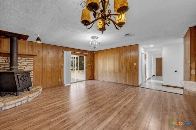 unfurnished living room featuring a wood stove, a notable chandelier, light hardwood / wood-style floors, and a textured ceiling