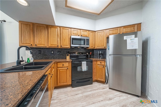 kitchen with sink, appliances with stainless steel finishes, tasteful backsplash, dark stone counters, and light hardwood / wood-style flooring