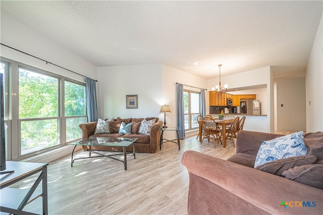 living room featuring a textured ceiling, a notable chandelier, a healthy amount of sunlight, and light hardwood / wood-style flooring