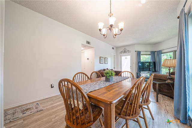 dining area featuring light hardwood / wood-style floors, a textured ceiling, and an inviting chandelier